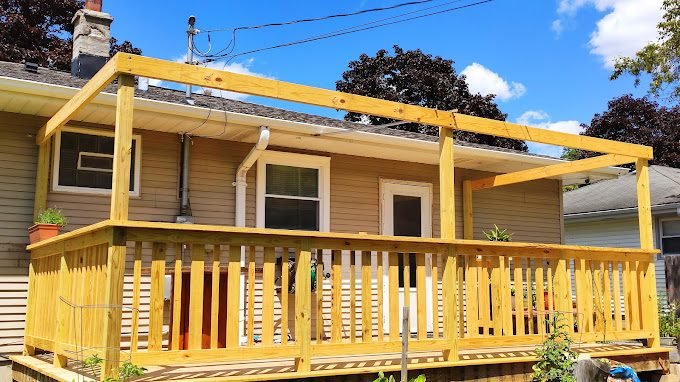 Cedar deck with a pergola frame overhead, freshly built onto the back of a home