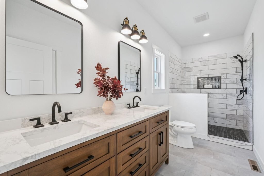 Bathroom with a wood double vanity, stone counter, and a tiled walk-in shower