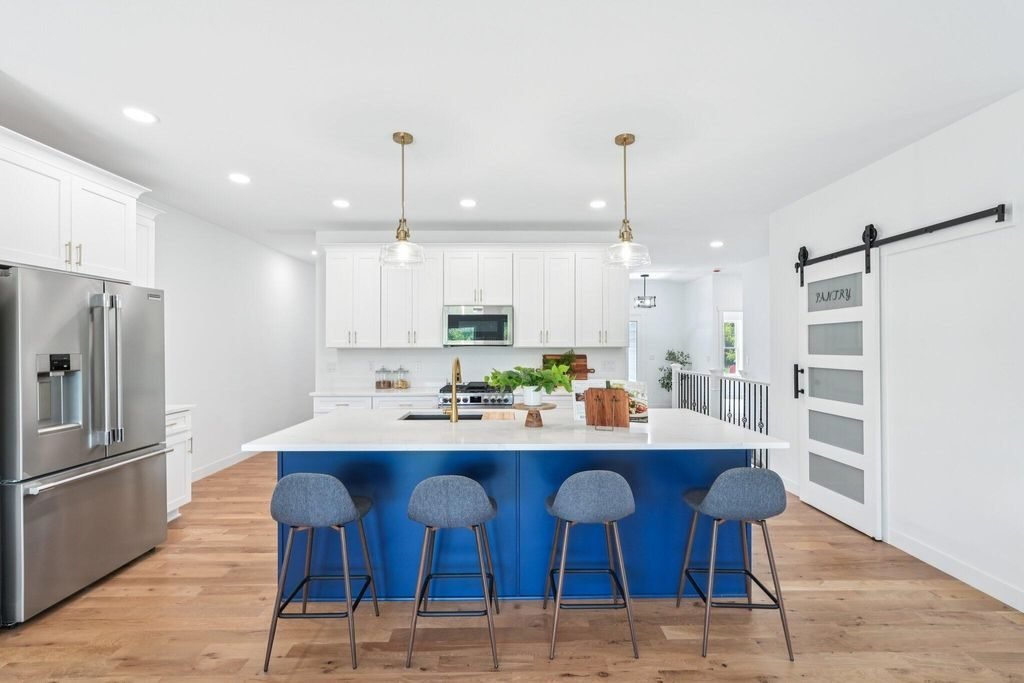 White kitchen with a navy island, pendant lighting, and a sliding barn door to the pantry