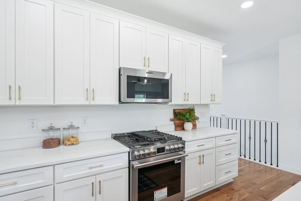Range wall with white shaker cabinetry and brass hardware, beside the stair rail