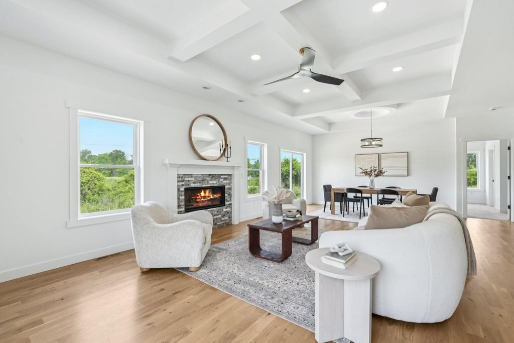Living room with a coffered ceiling, stone fireplace, and windows facing open country